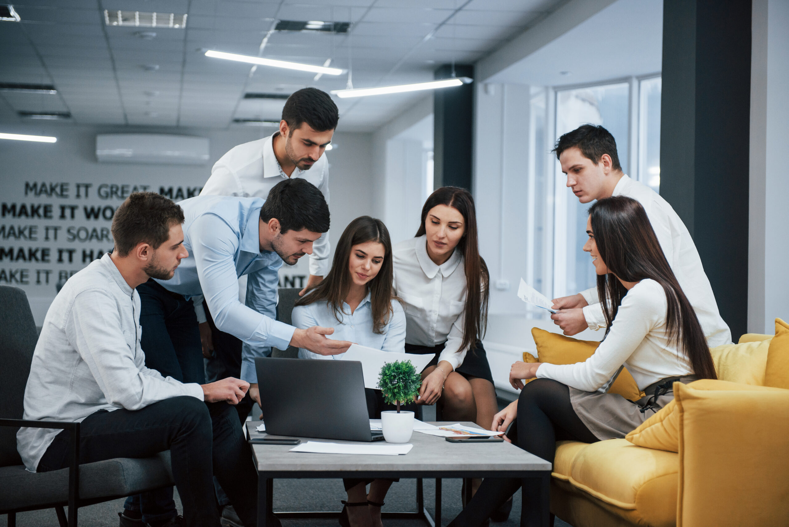 Guy shows document to a girl. Group of young freelancers in the office have conversation and working.